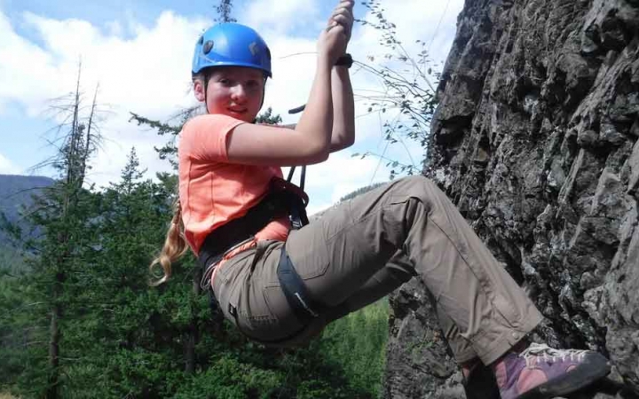 an outward bound student sits back on the ropes suspending them while rock climbing